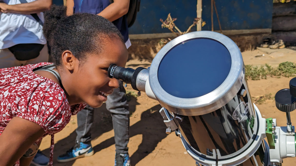 Une petite fille malgache regarde dans un télescope l’image du Soleil