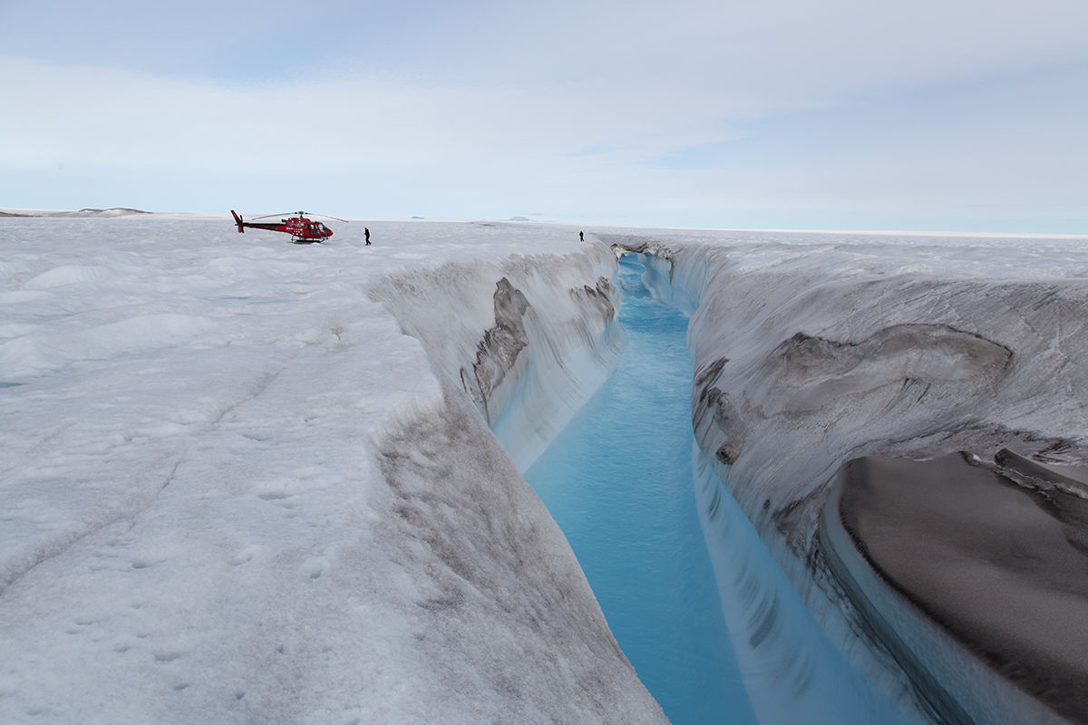 Hélicoptère posé près d’une rivière drainant un lac formé à la surface du glacier de Zachariæ Isstrøm, au nord du Groenland. © Romain MILLAN / Anders Anker BJØRK / IGE / University of Copenhagen / CNRS Images 