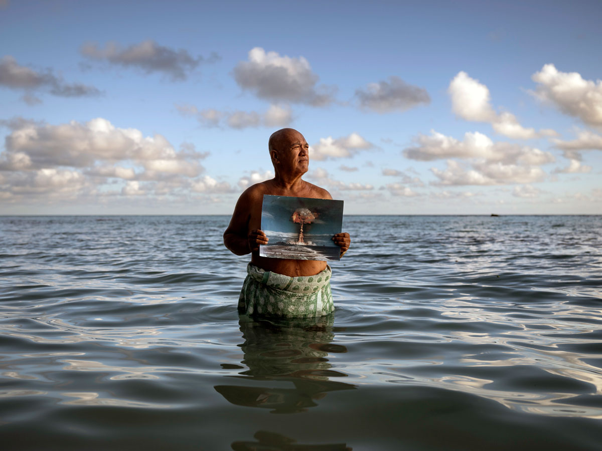 Angelo Tehuira-Hioe, 64 ans, tient une photo d’une explosion nucléaire © Adam Ferguson / The New York Times-Redux / RÉA