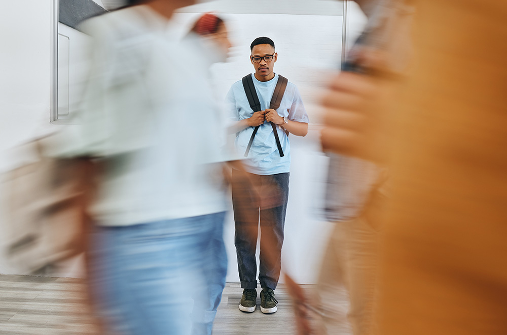 Jeune homme à l'arrière plan affichant une mine triste alors que des figures flous passent devant lui en l'ignorant