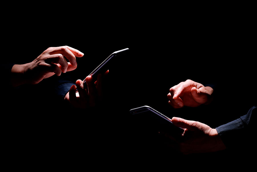 Deux paires de mains éclairées, sur fond noir, utilisent chacune un téléphone