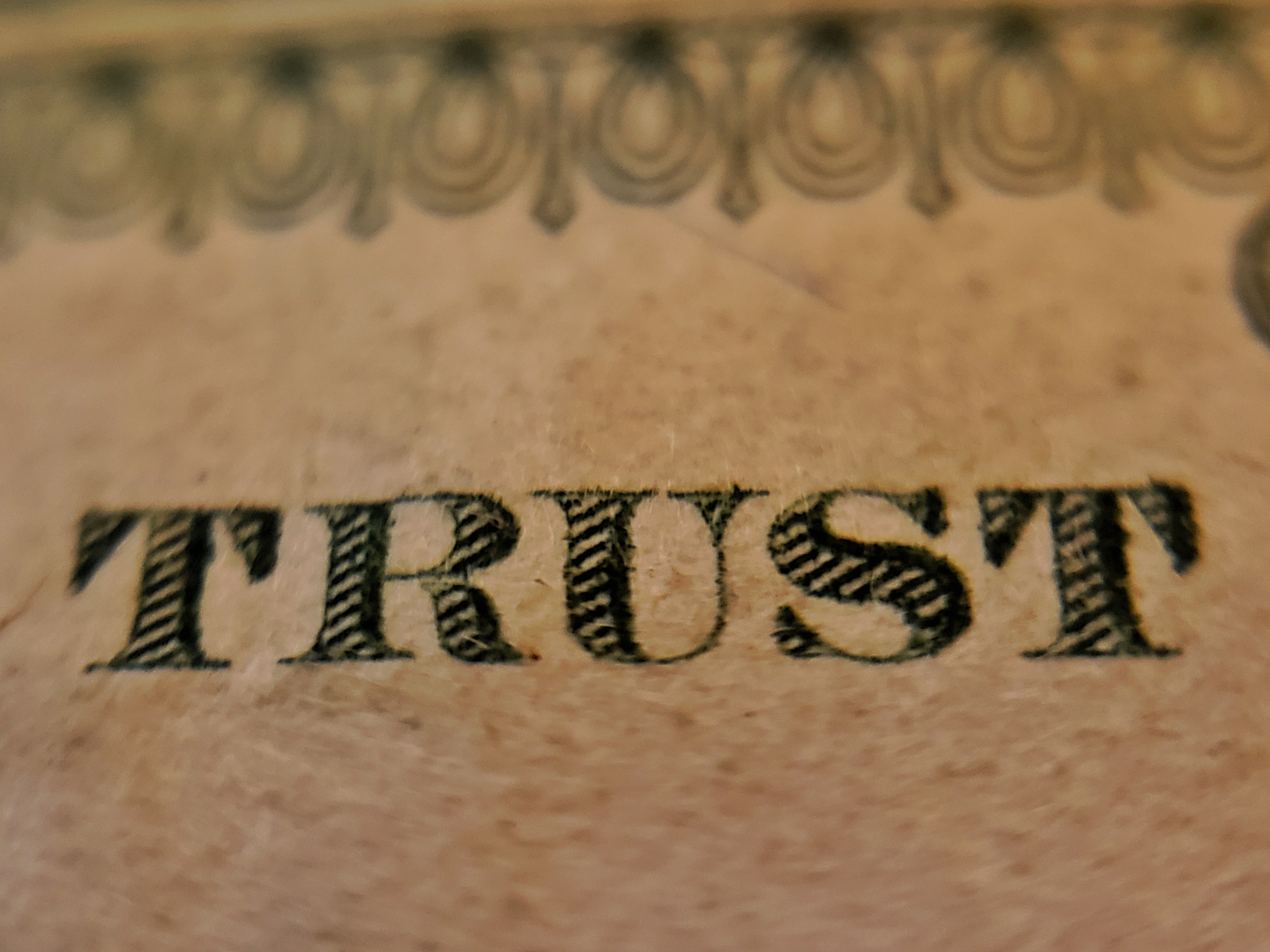 Photo d'un billet de banque américain, avec un zoom sur la partie "trust" de la devise "in god we trust" pour souligner la question de la confiance dans les investissements des banques