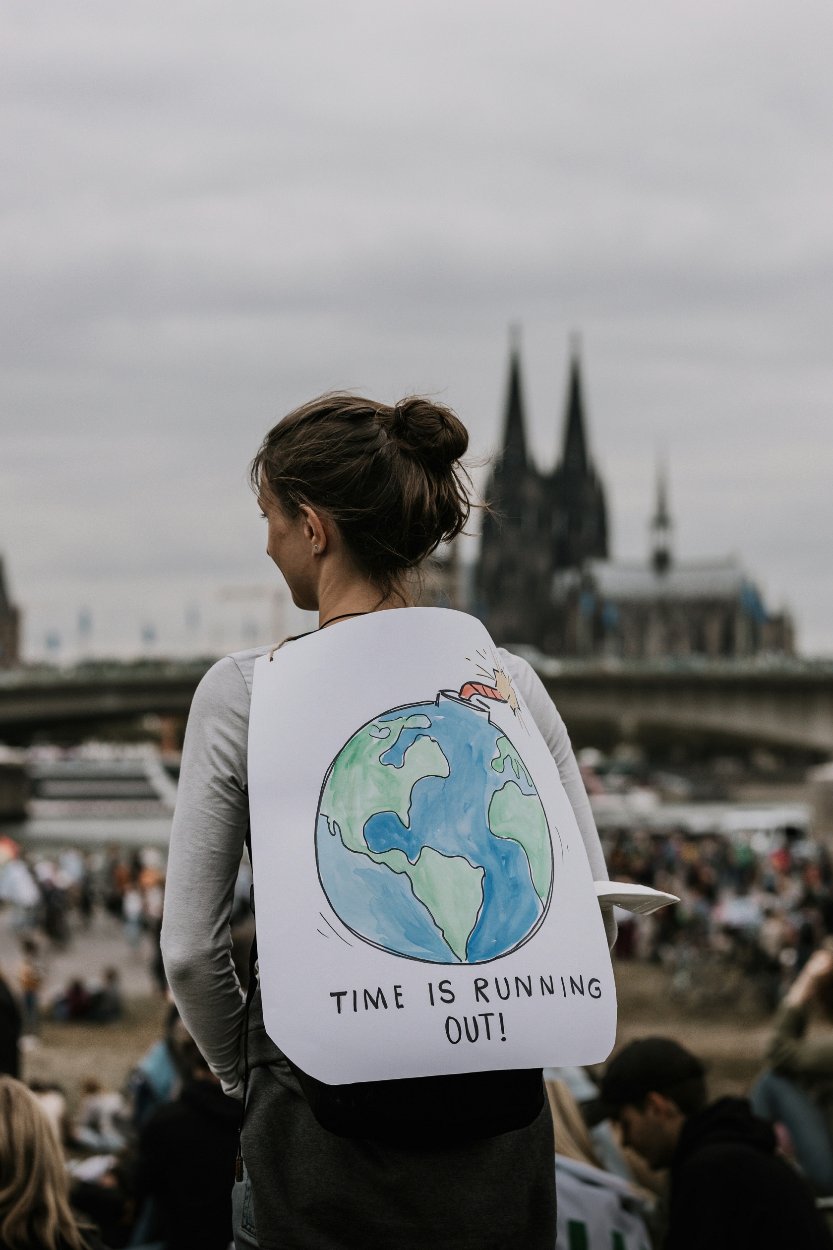 Vue de dos d’une femme manifestant avec un panneau signifiant « le temps est compté pour la planète ».