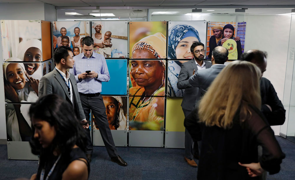 Des hommes et des femmes d’origines diverses devant un mur de photos de femmes.