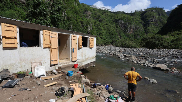 Un habitant les pieds dans l’eau près d’une maison endommagée par les crues provoquées par le cyclone Garance en mars 2025