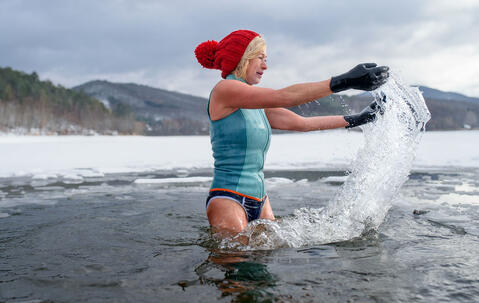 Une femme avec des gants et un bonnet rouge se baignant dans un lac gelé