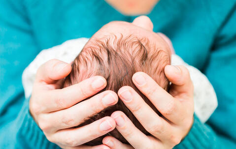 Deux mains tiennent la tête d’un bébé