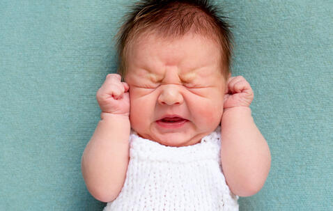 Un bébé pleurant, les poings sur les oreilles et les yeux froncés