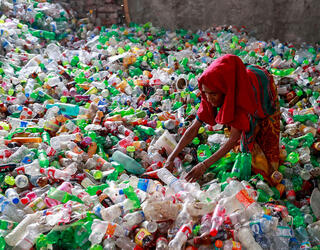 Une femme trie des bouteilles en plastique avant leur recyclage, son enfant en arrière-plan sur l’amoncellement de bouteilles