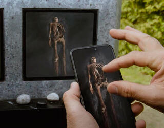 image du film où une main touche un téléphone qui montre l’intérieur de la tombe et on voit le squelette