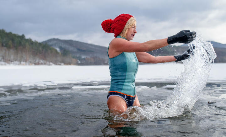 Une femme avec des gants et un bonnet rouge se baignant dans un lac gelé