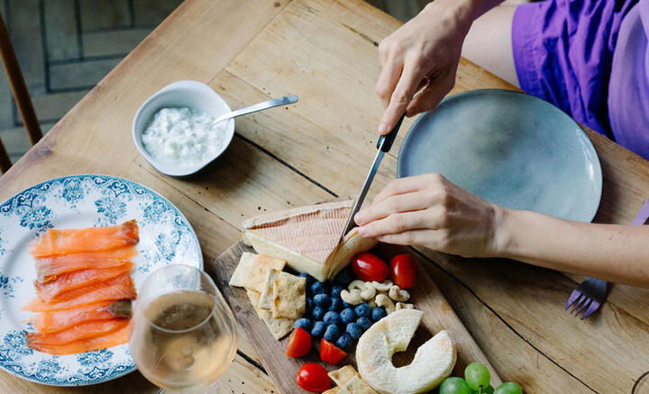 Une personne attablée découpe du fromage sur un plateau 