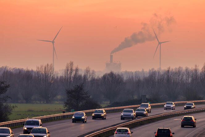 Voitures sur une autoroute en Europe, et en arrière-plan, des fumées d’usine et des éoliennes