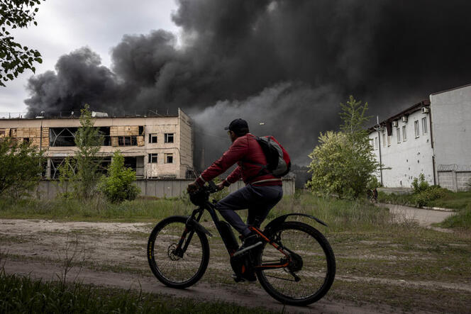 Un homme à vélo passe devant un bâtiment d’où s’échappe une épaisse fumée noire