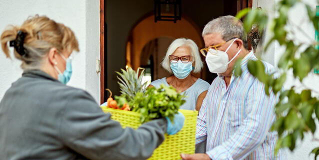 Une femme livre des légumes à un couple âgé ; ils portent des masques anti covid