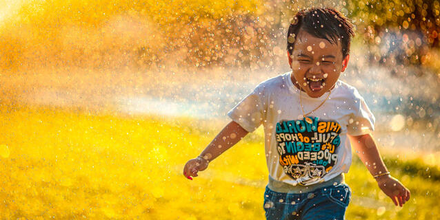 ©Mi Pham / Unsplash un enfant court en riant, arrosé par un jet d’eau