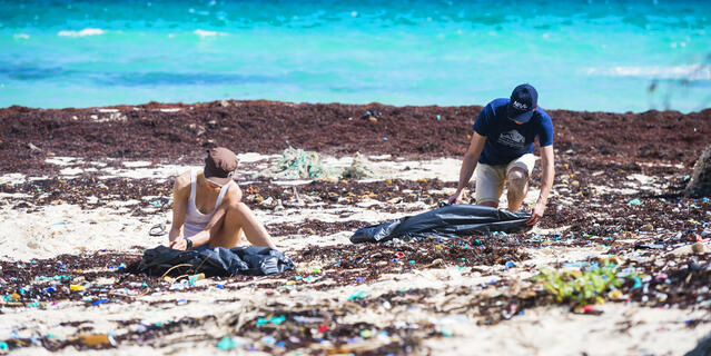 Deux personnes accroupies sur une plage jonchée de plastique.