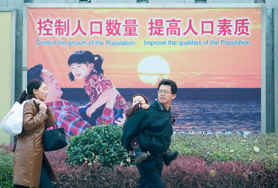 Un couple et leur enfant passe devant une affiche qui promeut l’enfant unique