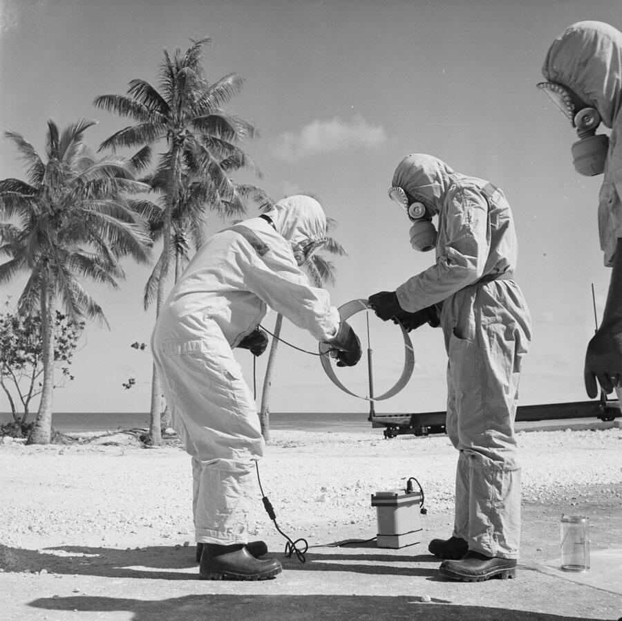 Personnel en tenue de protection testent la radioactivité de matériel avec un détecteur après un tir d’essai nucléaire, Centre d’expérimentations du Pacifique (CEP), juillet 1966. © Robert Antoine / ECPAD / Défense / F 66-272 R12