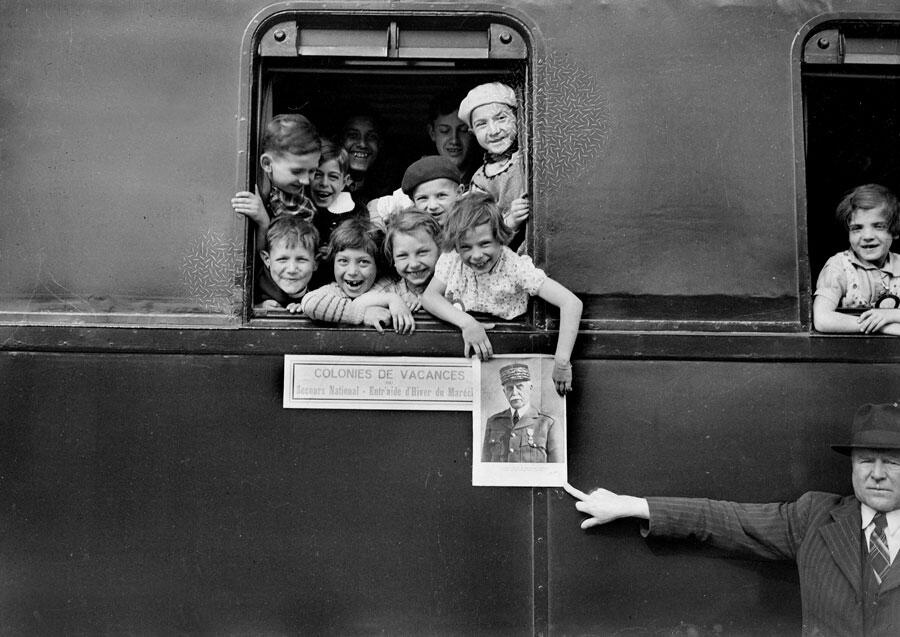 des enfants à la fenêtre d'un train sont heureux de partir en colonie de vacances, et tiennent une photo de Pétain.