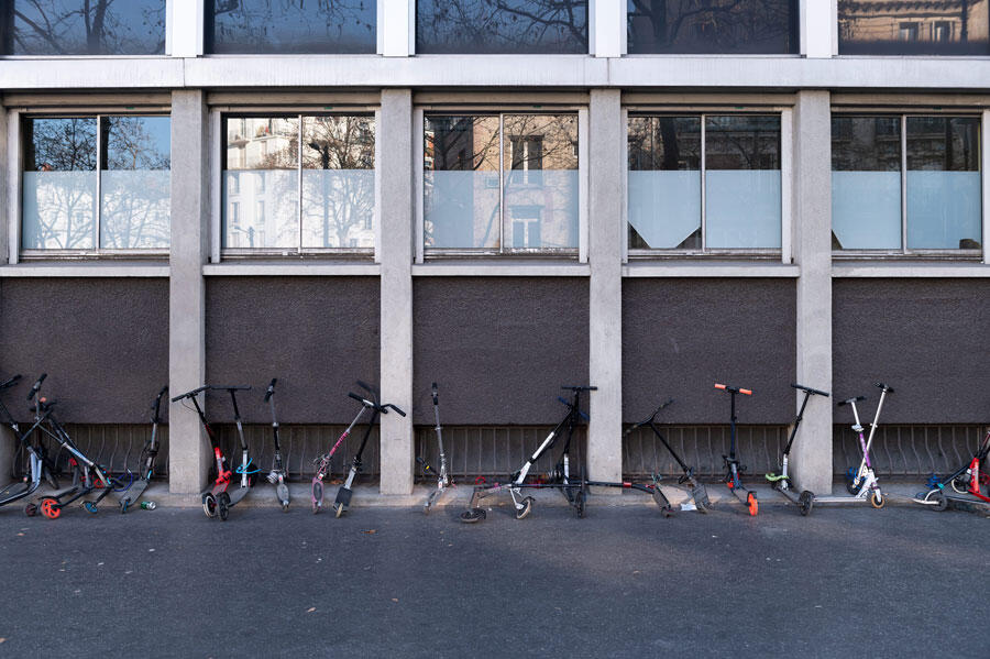 Des trottinettes alignées devant un établissement scolaire.