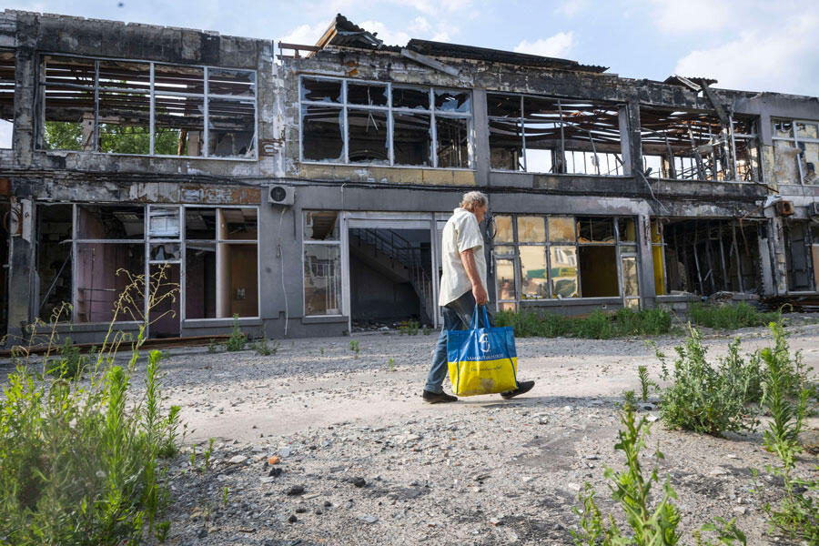 Un homme portant un sac de courses aux couleurs du drapeau ukrainien passe devant un bâtiment détruit. 