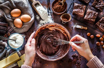 ©fcafotodigital / iStockphoto.com Des mains mélangent une pate chocolatée avec un batteur, les ingrédients du gâteau sont disposés autour