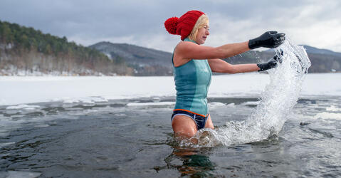 Une femme avec des gants et un bonnet rouge se baignant dans un lac gelé