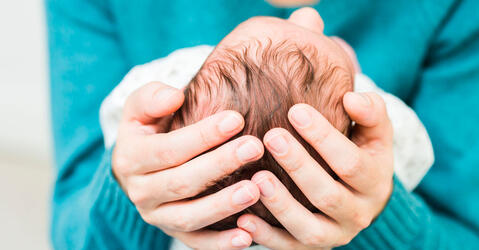 Deux mains tiennent la tête d’un bébé