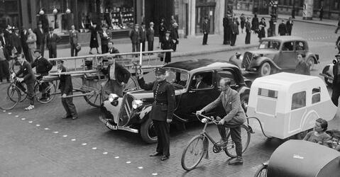Dans une rue de Paris en 1940, un agent de police retient derrière une ligne de clous divers engins roulants