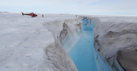 Hélicoptère posé près d’une rivière drainant un lac formé à la surface du glacier de Zachariæ Isstrøm, au nord du Groenland. © Romain MILLAN / Anders Anker BJØRK / IGE / University of Copenhagen / CNRS Images 