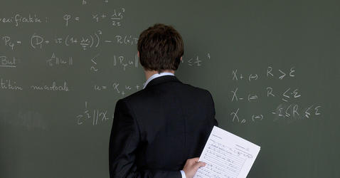 Homme face à un tableau vert sur lequel sont inscrit des équations.