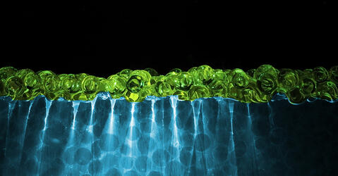 Phénomène d'iso-indice : billes transparentes vertes dans un fluide bleu, la lumière les traverse sans être déformée.