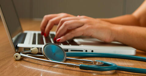 des mains tapent sur un clavier, un stéthoscope au premier plan