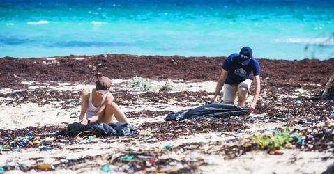 Deux personnes accroupies sur une plage jonchée de plastique.
