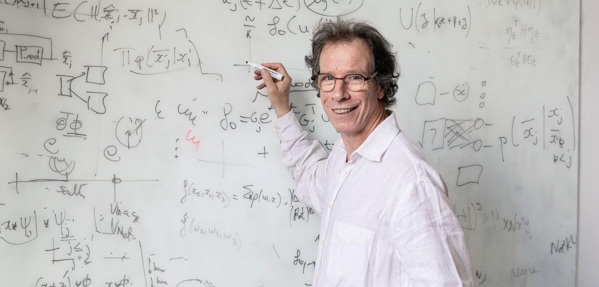 ©Frédérique Plas / CNRS Images Portrait de Stéphane Mallat devant un tableau blanc couvert de formules mathématiques