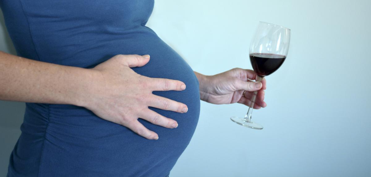 Une femme enceinte tient un verre d'alcool à la main.