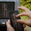 image du film où une main touche un téléphone qui montre l’intérieur de la tombe et on voit le squelette