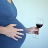 Une femme enceinte tient un verre d'alcool à la main.