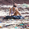 Deux personnes accroupies sur une plage jonchée de plastique.